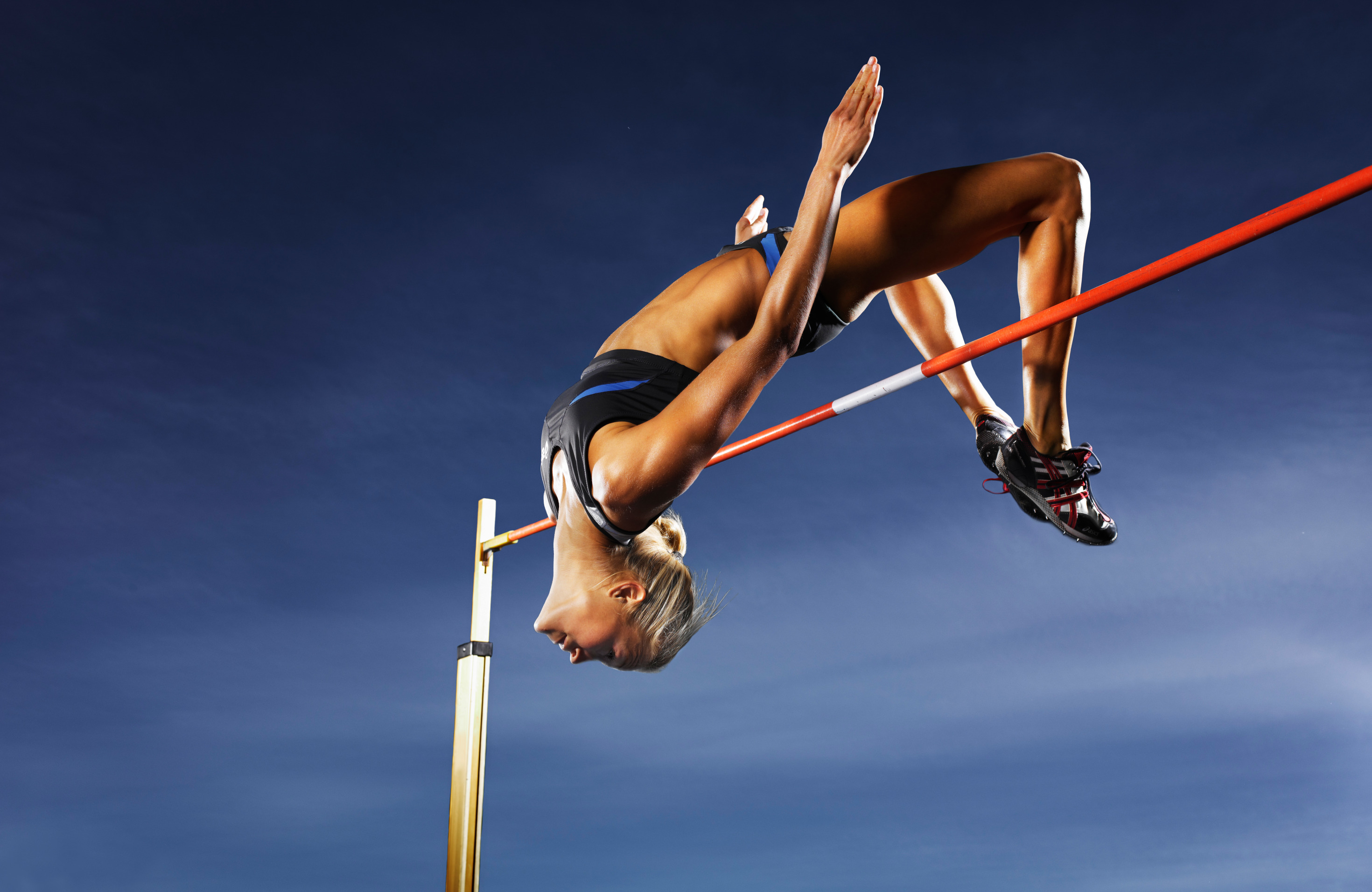 Female athlete performing high jump against blue sky